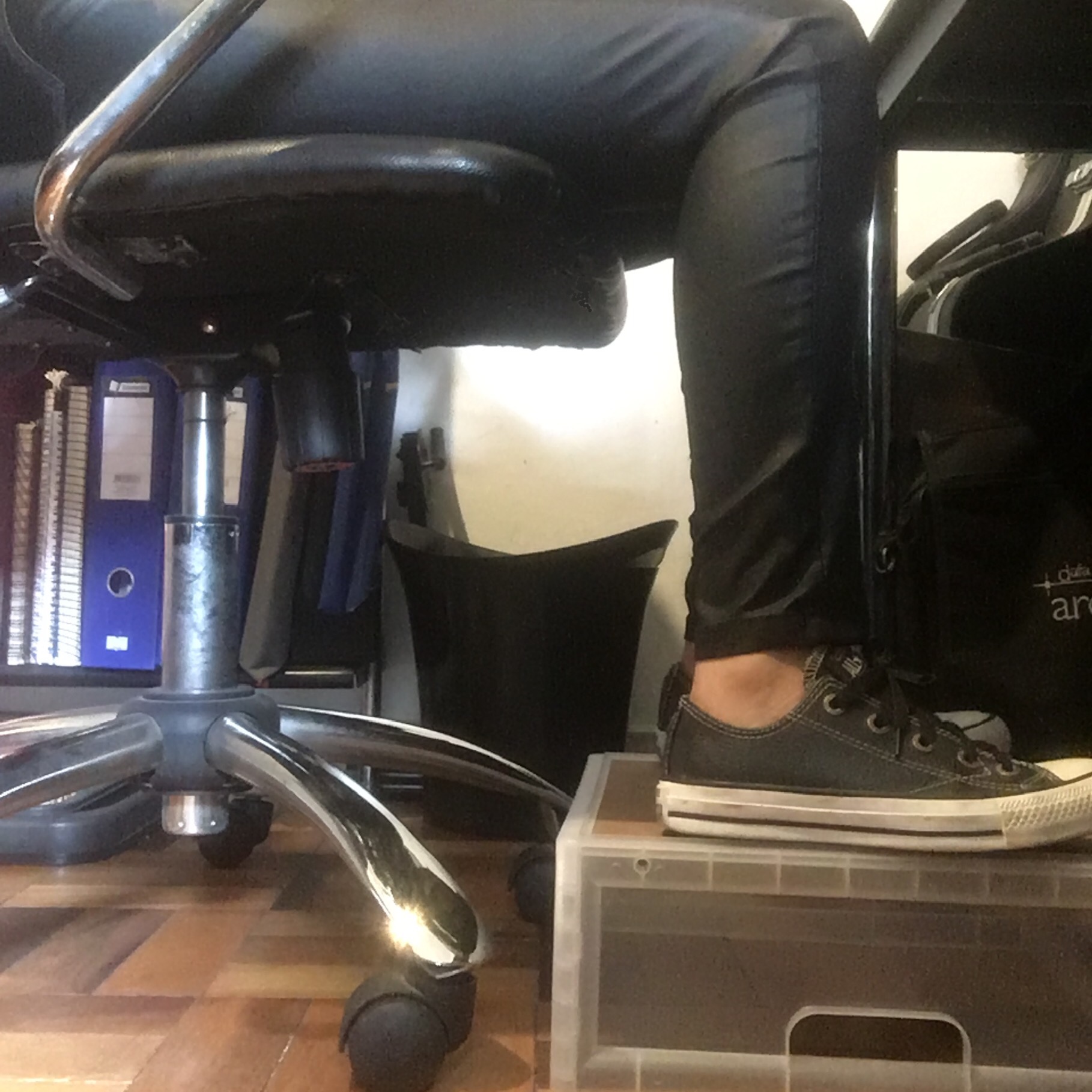 Imagem parcial de uma pessoa sentada, mostrando as pernas e os pés, apoiados em caixa resistente.